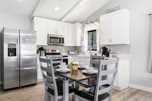 A modern kitchen with white cabinetry, stainless steel appliances, and a dining area with a wooden table and chairs. - Walk to the Beach, North Myrtle Beach Getaway (North Myrtle Beach)