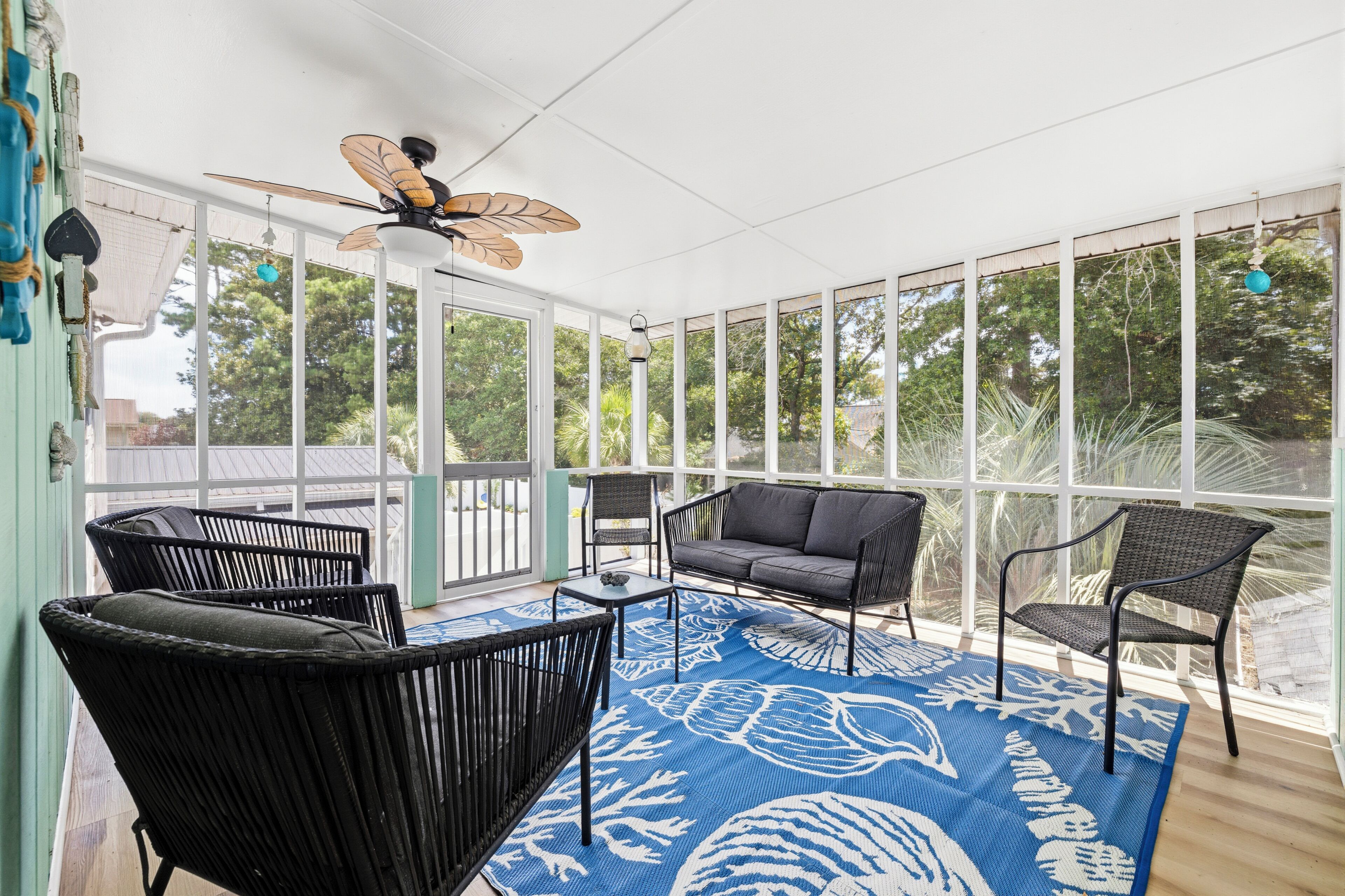 A sunroom with a ceiling fan, large windows, and black wicker furniture.