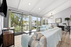 A spacious living area with a large window, a sofa, a coffee table, and a television. - Walk to the Beach, North Myrtle Beach Getaway (North Myrtle Beach)