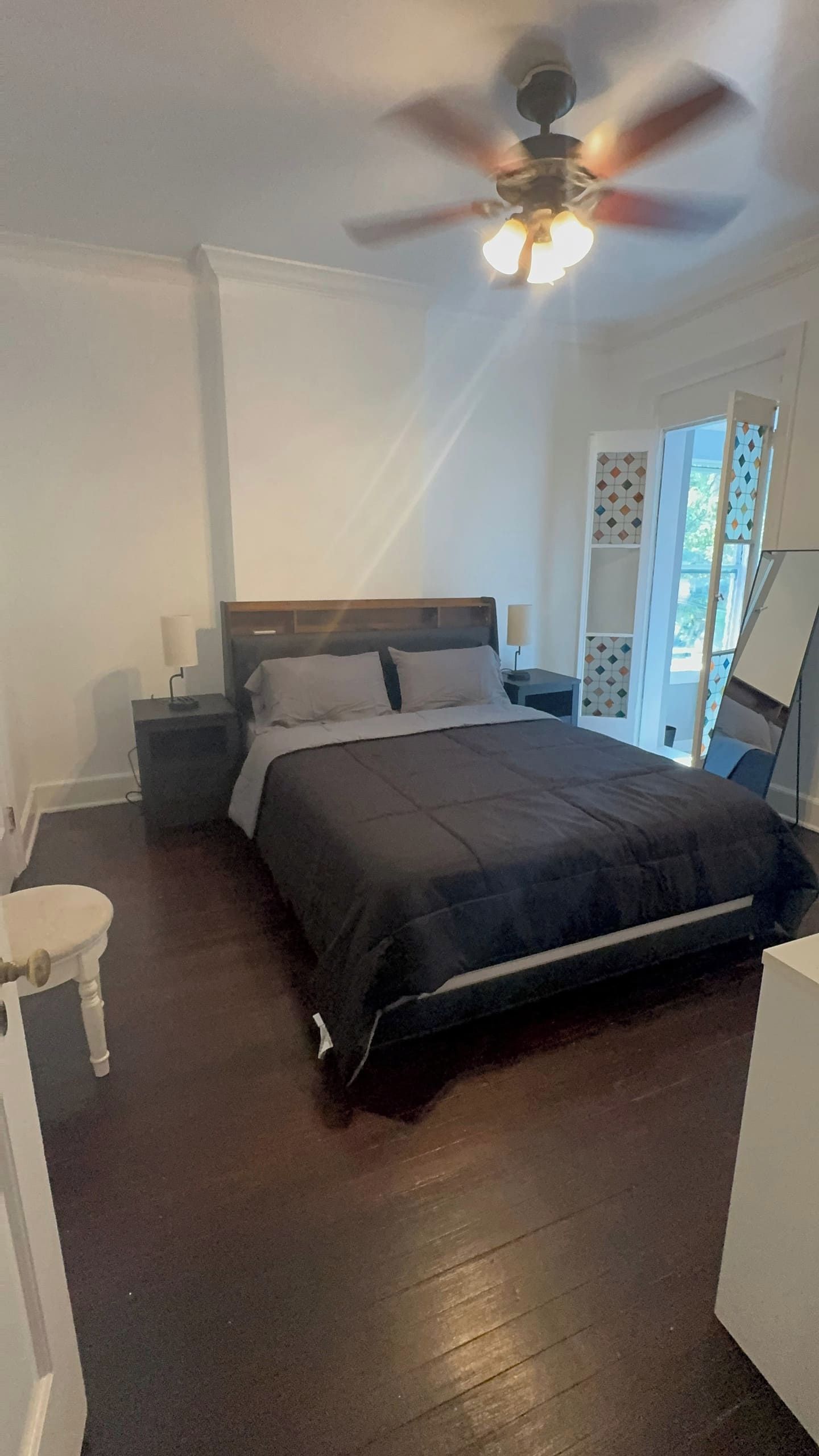 A bedroom with a bed, bedside tables, a ceiling fan, and a window with a view.