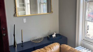 Et værelse med et stort spejl, en brun lædersofa, et lille bord med dekorative genstande og et vindue med udsigt.