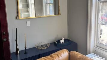 Une pièce dotée d’un grand miroir, d’un canapé en cuir marron, d’une petite table ornée d’objets décoratifs et d’une fenêtre donnant sur l’extérieur.