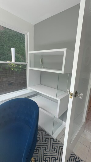 Ein Zimmer mit blauem Sessel, einer weißen, fest eingebauten Schrankwand und einem Fenster mit Blick auf Grünflächen.