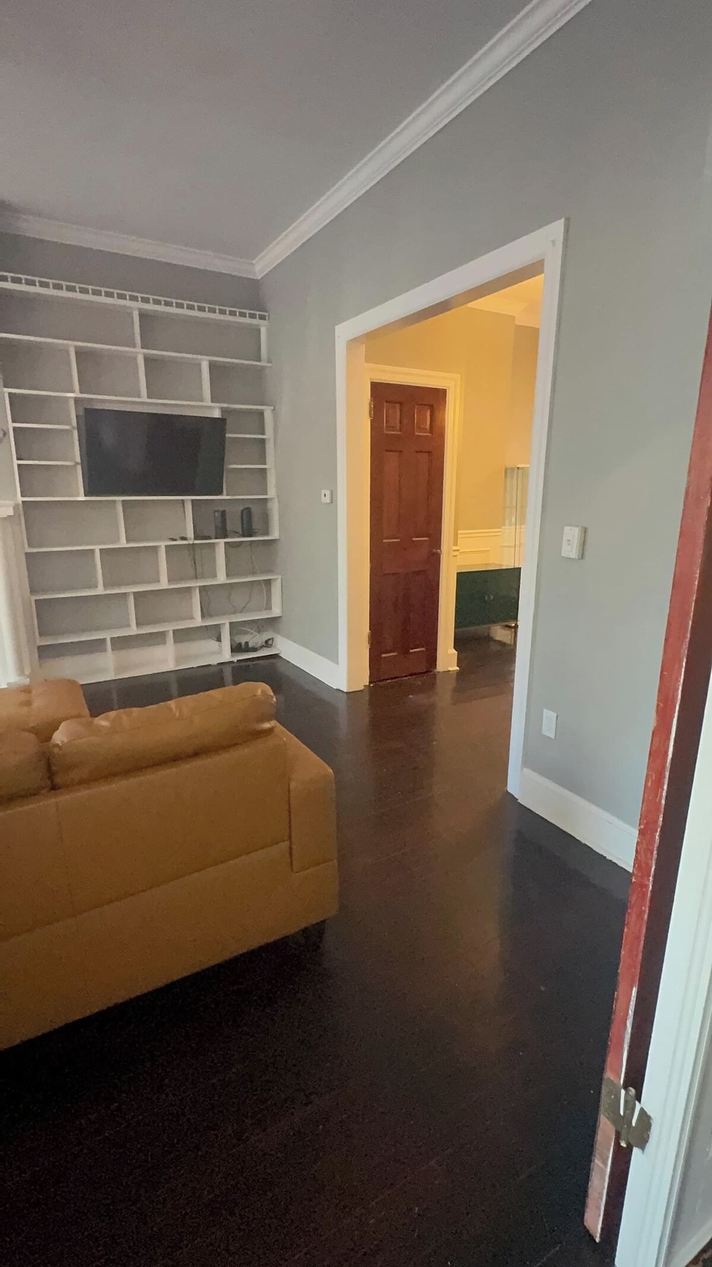 A living room with a dark hardwood floor, a beige sofa, and a mounted flat-screen TV on a white wall.