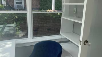 A room with a ceiling fan, a blue chair, a patterned rug, and a view of a brick wall and greenery outside.