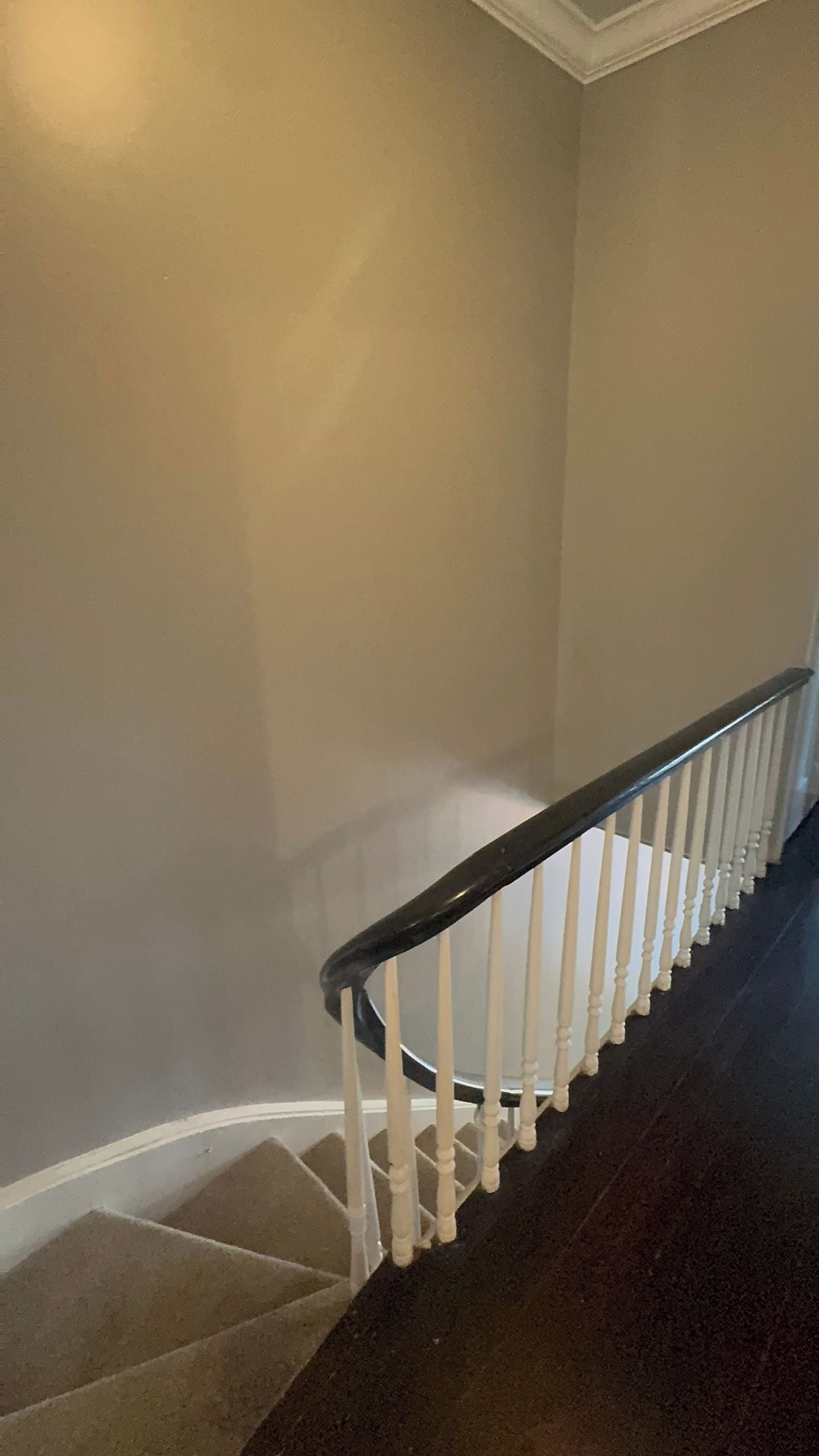 A staircase with white balusters and a black handrail, leading to a landing with a white baseboard.