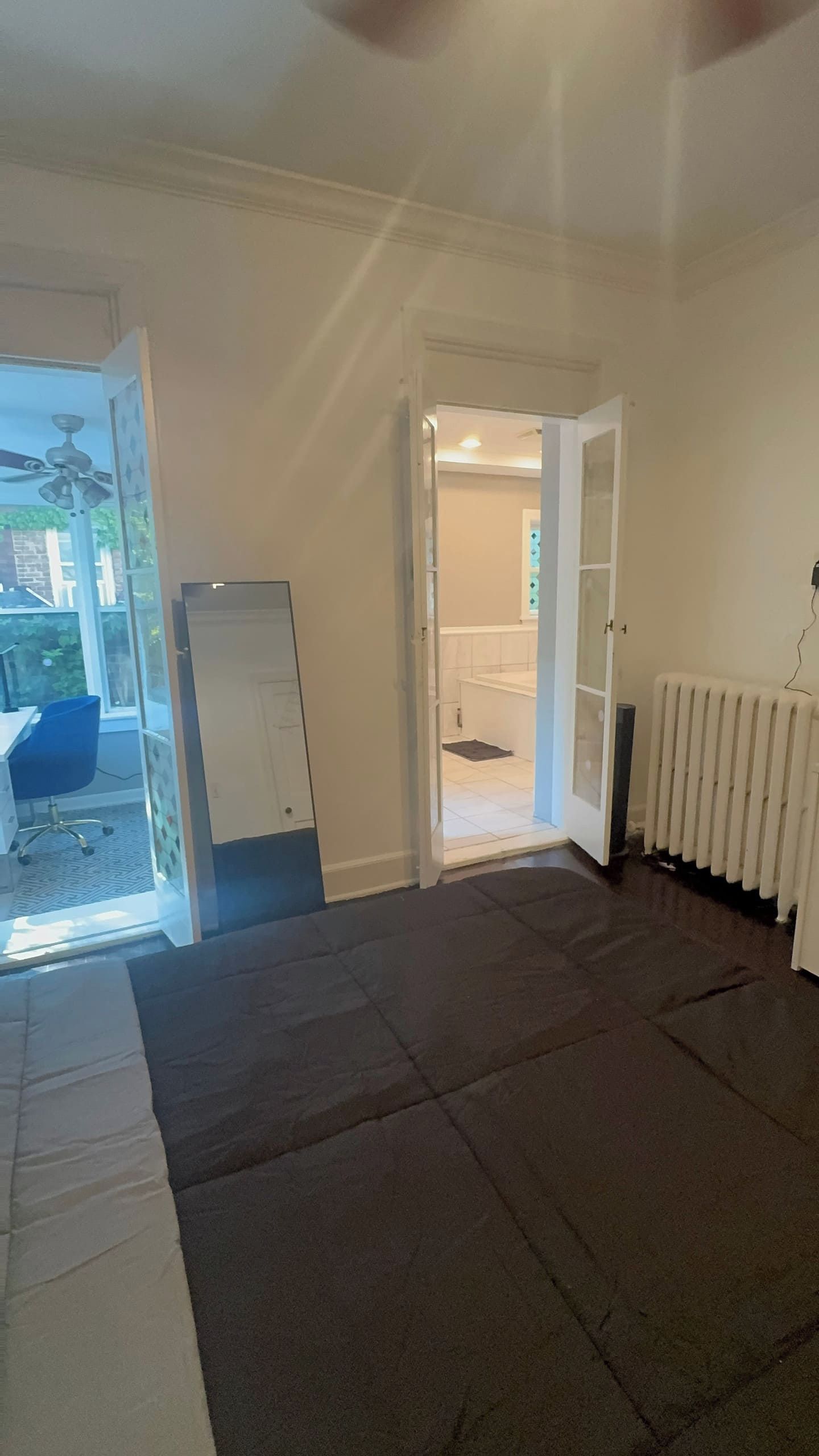 A room with a large window, a radiator, and a door leading to another room.