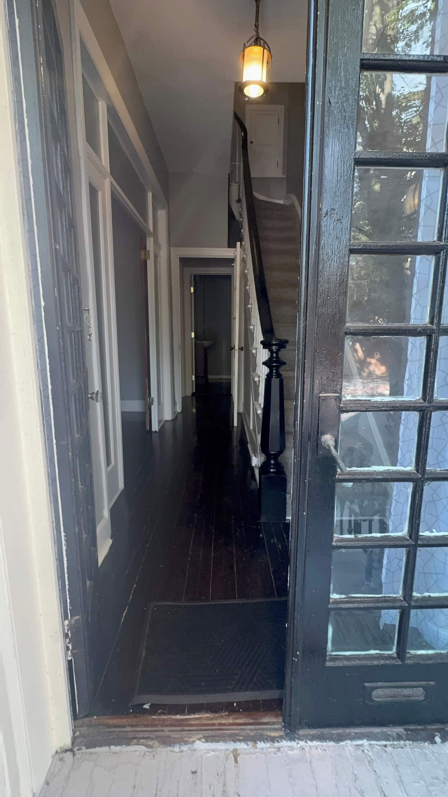 A hallway with a staircase leading to a second floor, a door with glass panels, and a hanging light fixture.