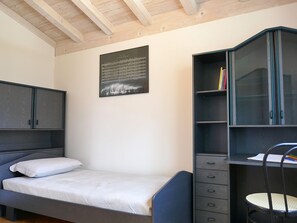A bedroom with a bed, a desk with drawers, a chair, and a wall-mounted shelf. - Casa Alenzino by Interhome (Corzoneso)