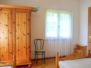 Ein Schlafzimmer mit Holzschrank, Bett, Stuhl und einem Fenster mit transparenten Vorhängen.