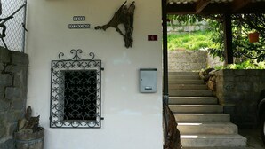 Entrada de um edifício com portão de metal, placa de madeira e escadaria que leva a uma área coberta.