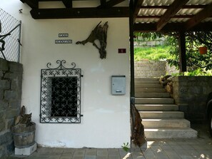 Ein Gebäudeeingang mit einem Metallgitter, einem hölzernen Schild und einer Treppe, die zu einem überdachten Bereich führt.