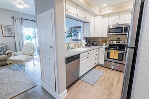 Une cuisine moderne avec des meubles blancs, des appareils en acier inoxydable et un coin repas agrémenté d’un tapis de couleur claire et d’une chaise blanche.