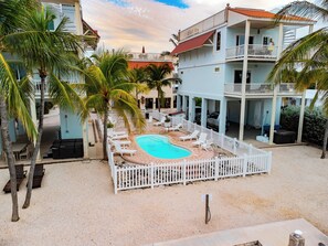 A pool area with lounge chairs and a white fence, surrounded by palm trees and buildings. - *NEW* Villa De Madera~Dock!~Pool!~Kayaks!~Grill! (Marathon)