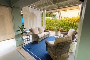 Un espace extérieur aménagé, abrité et doté de meubles en osier et d’un tapis bleu.