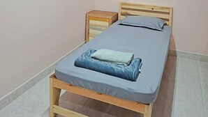 A single bed with a wooden frame, a nightstand, and a wall socket.