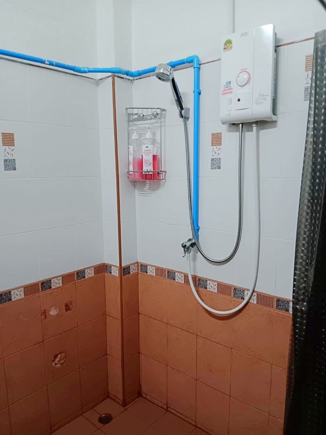 A shower with a blue pipe, a glass soap dispenser, and a control unit on the wall.