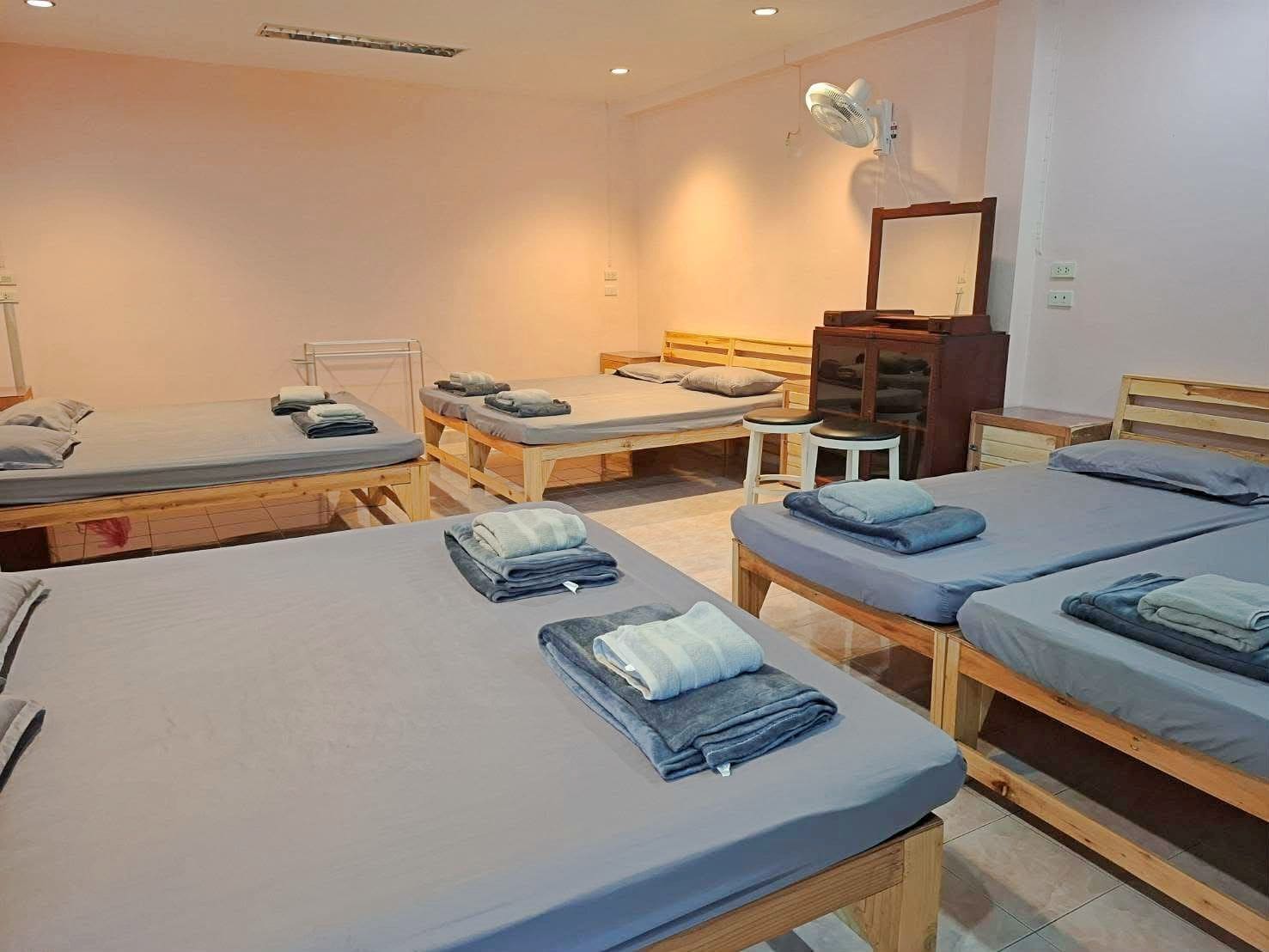 Habitación de hotel con cuatro camas individuales, un taburete pequeño, un espejo y un ventilador.