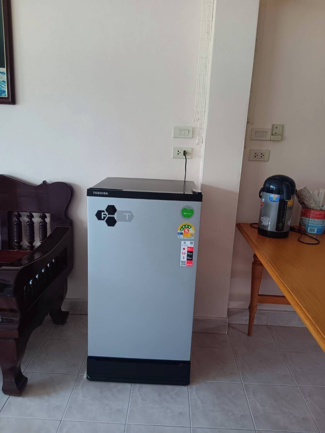 Un refrigerador compacto con el logotipo de Toshiba, un enchufe y una cafetera sobre una mesa de madera.