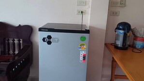 A compact refrigerator with a Toshiba logo, a power outlet, and a coffee maker on a wooden table.