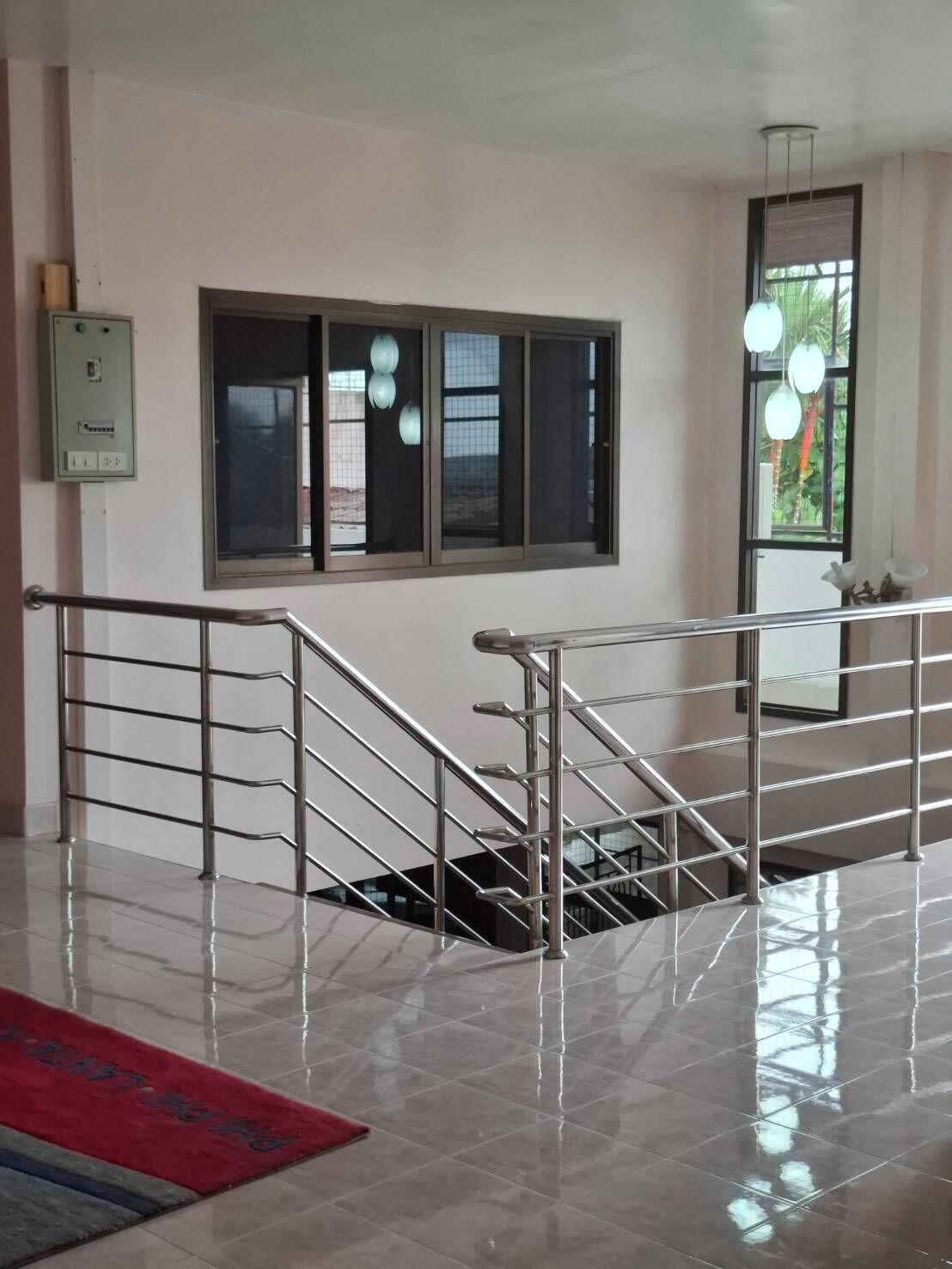 A staircase with metal railings leading to an upper floor, a window with blinds, and a light fixture above.