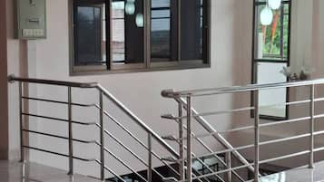 A staircase with metal railings leading to an upper floor, a window with blinds, and a light fixture above.