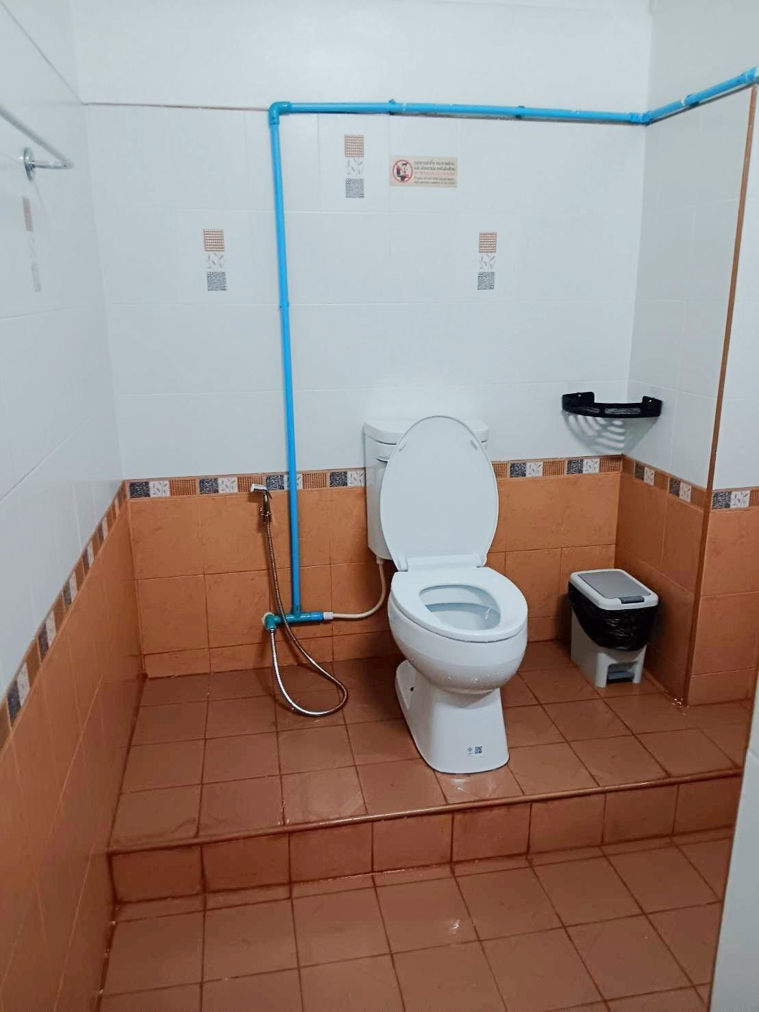 A small bathroom with a toilet, a trash bin, and a shower area.