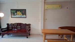 A room with a dark wooden sofa, a wooden table, and a bench. There is a painting on the wall and an air conditioning unit mounted above the table.