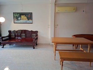 Una habitación con un sofá de madera oscura, una mesa de madera y un banco. Hay un cuadro en la pared y un equipo de aire acondicionado montado sobre la mesa.