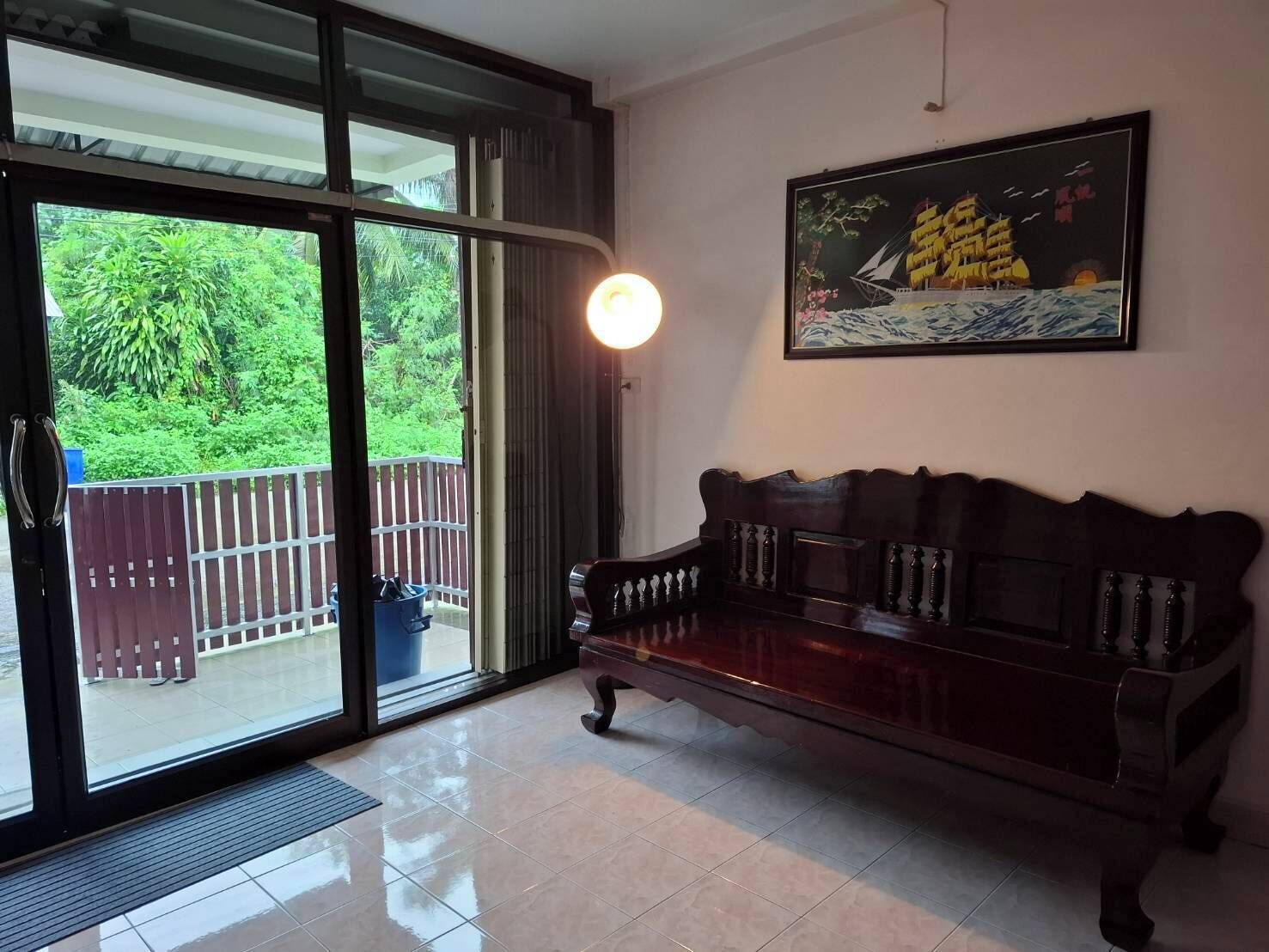 A room with a dark wooden sofa, a glass door leading to a balcony, and a framed picture on the wall.