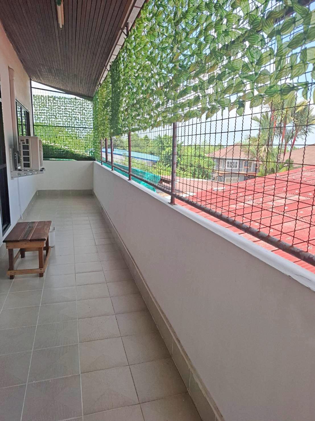 A balcony with a view of a red-roofed area, a wooden bench, and a wall-mounted air conditioning unit.