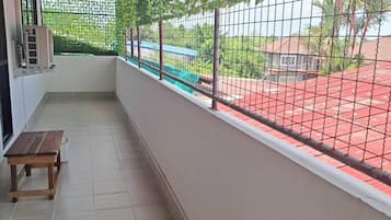 A balcony with a view of a red-roofed area, a wooden bench, and a wall-mounted air conditioning unit.