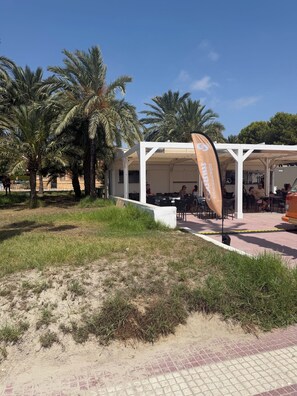 An outdoor seating area with tables and chairs, surrounded by palm trees and a white structure. - La Casa Alegría, a luxury 3-bedroom apartment (San Javier)
