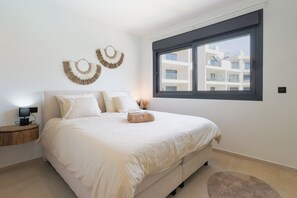 A bedroom with a bed, bedside table, lamp, wall decor, and a window with a view of buildings. - La Casa Alegría, a luxury 3-bedroom apartment (San Javier)