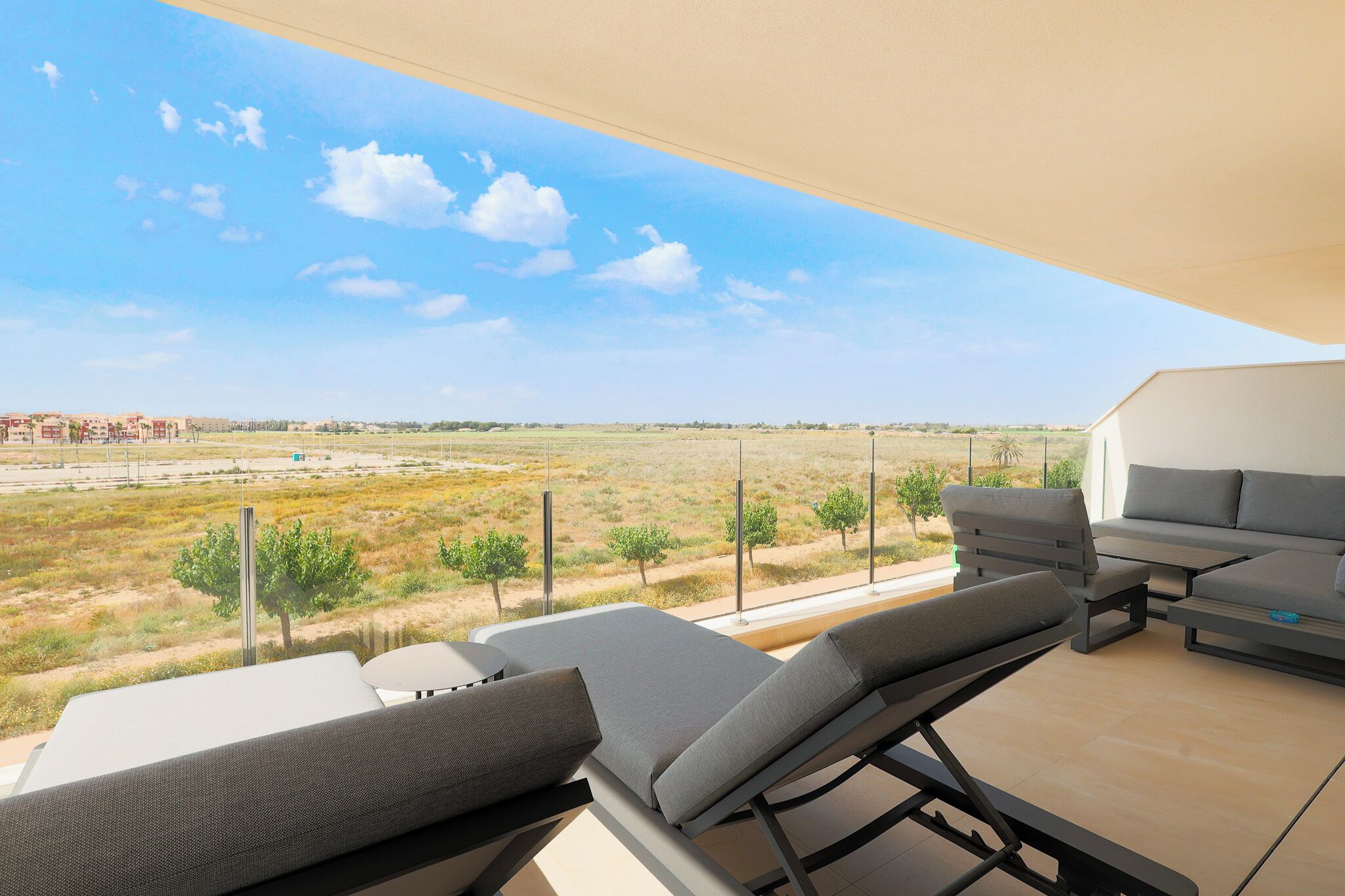 A balcony with a view of a flat landscape, a sofa, and a table.