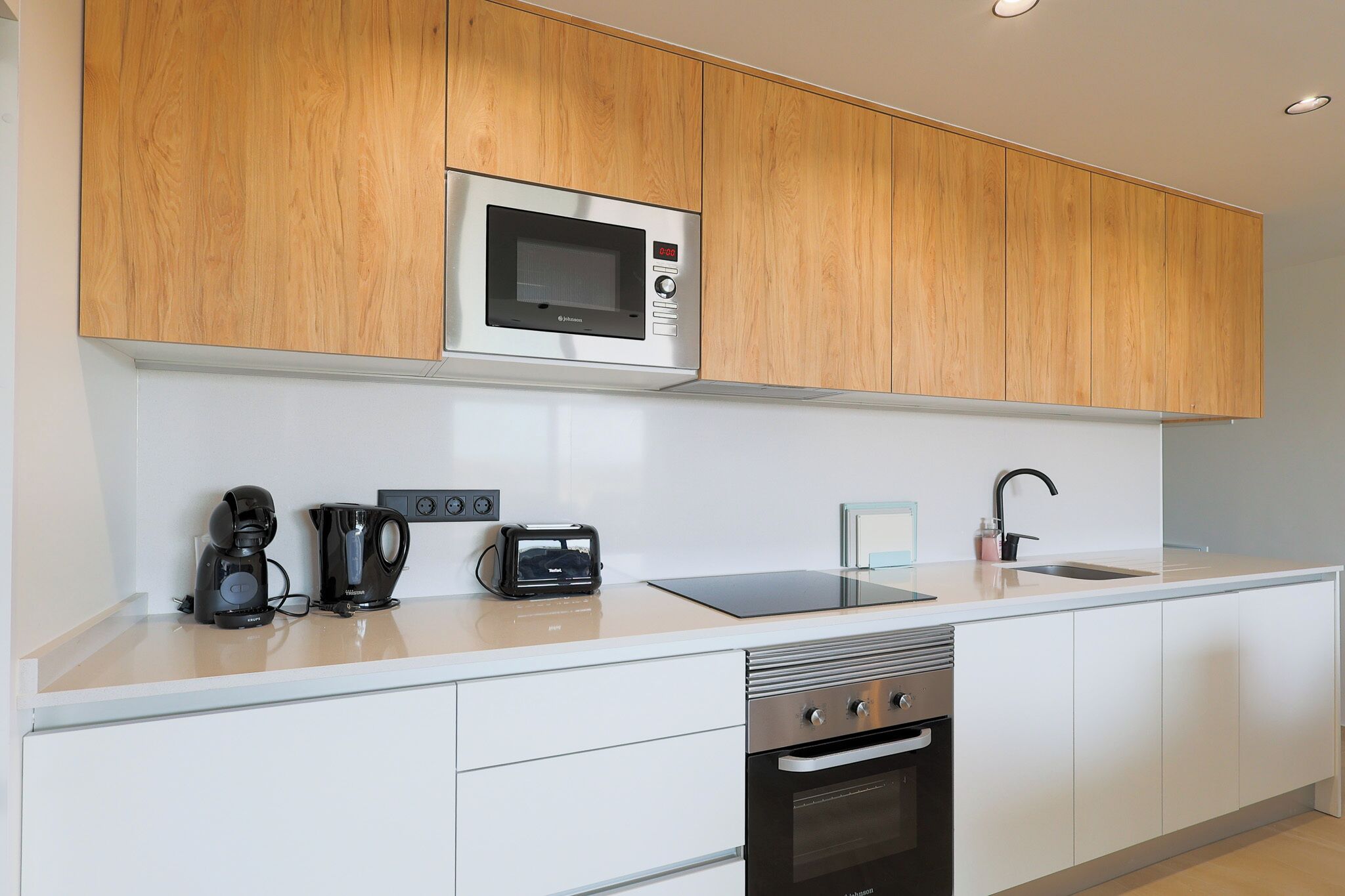 Una cocina moderna con armarios de madera, microondas integrado, cafetera, tostadora, lavavajillas y un lavabo.