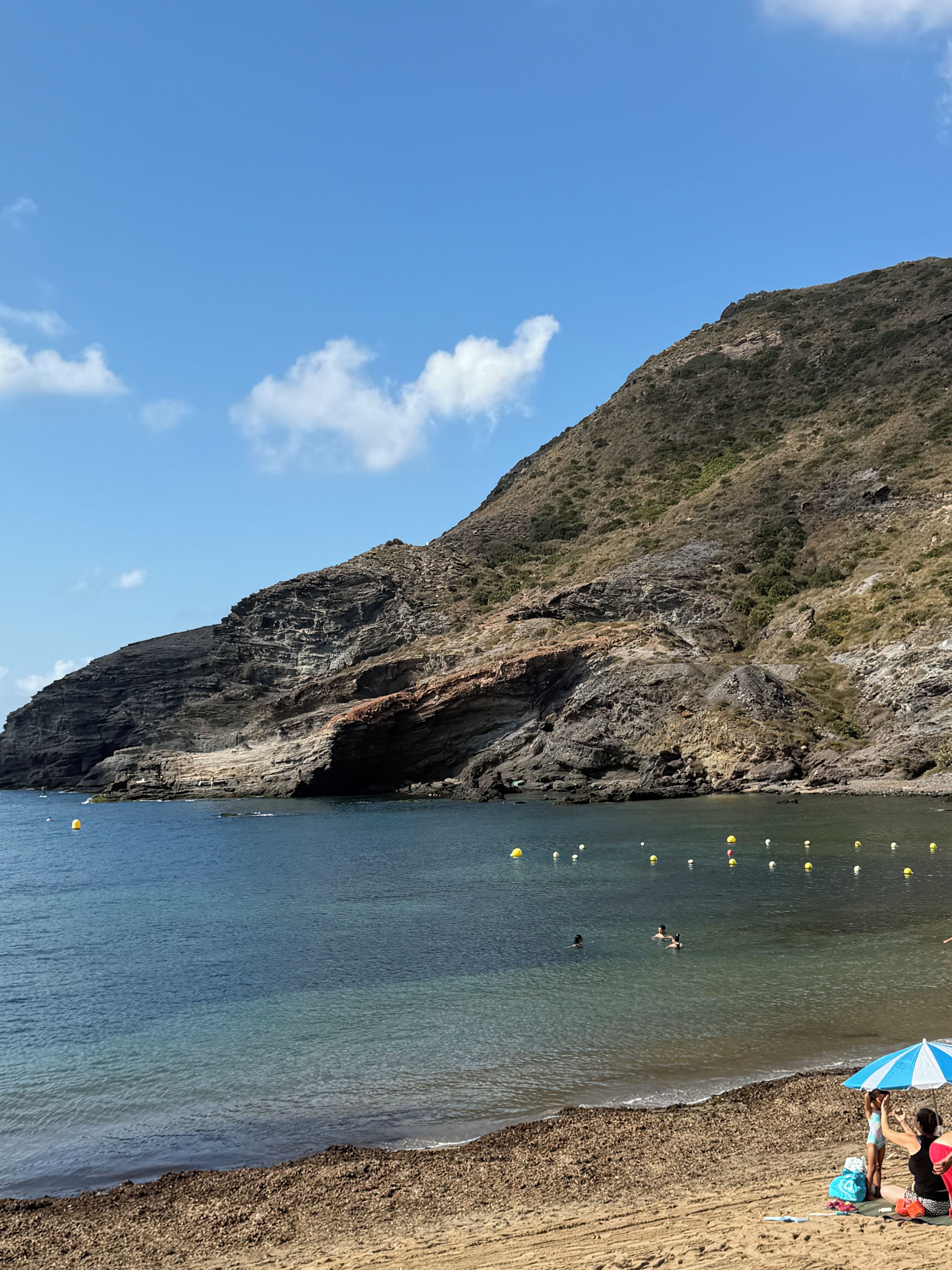 A beach with rocky cliffs, clear water, and a few people.