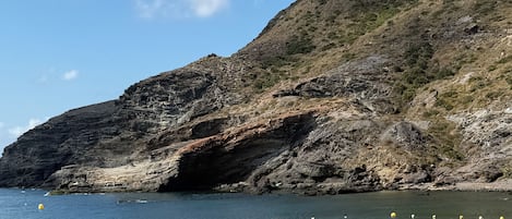 Una playa con acantilados rocosos, agua cristalina y algunas personas.
