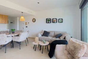 A modern living room with a sofa, two armchairs, a dining table with chairs, and a kitchen area in the background. - La Casa Alegría, a luxury 3-bedroom apartment (San Javier)