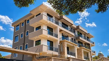 Un immeuble résidentiel à plusieurs étages, doté d’une façade en pierre, de nombreux balcons et surplombant un ciel dégagé.