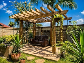 A covered patio area with a wicker bench, potted plants, and a pergola structure.