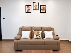 Un sofá marrón con cojines blancos en una habitación con suelo de madera y pared blanca.