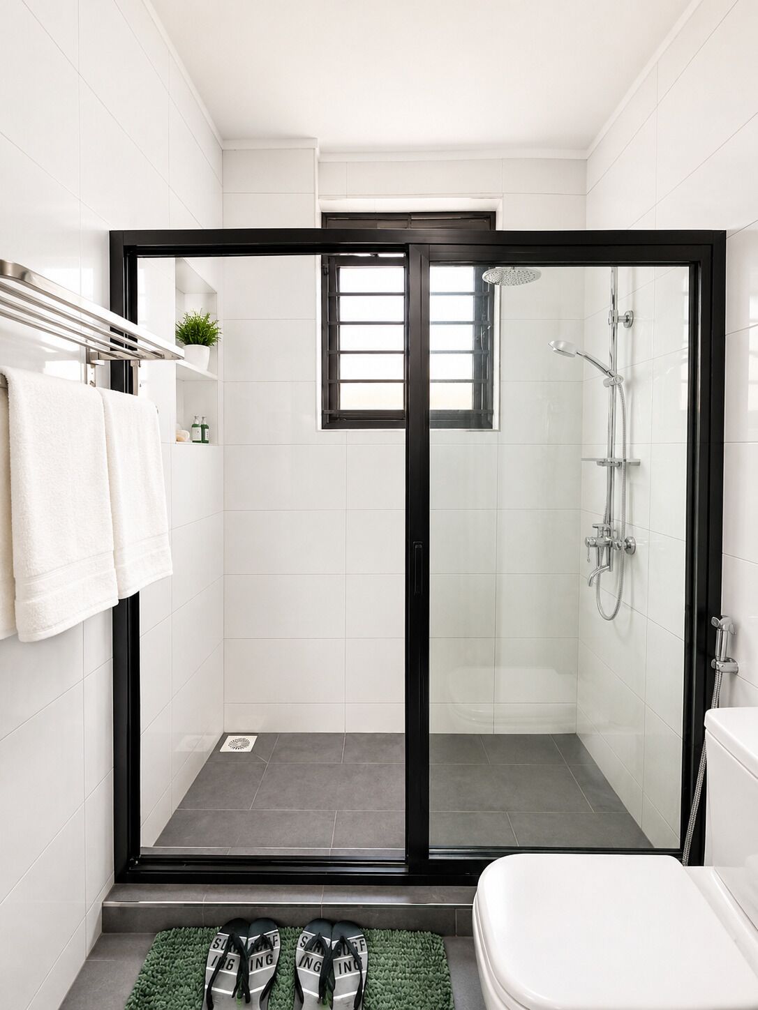 A modern bathroom with a glass-enclosed shower, white tiles, a toilet, and a pair of shoes on a mat.