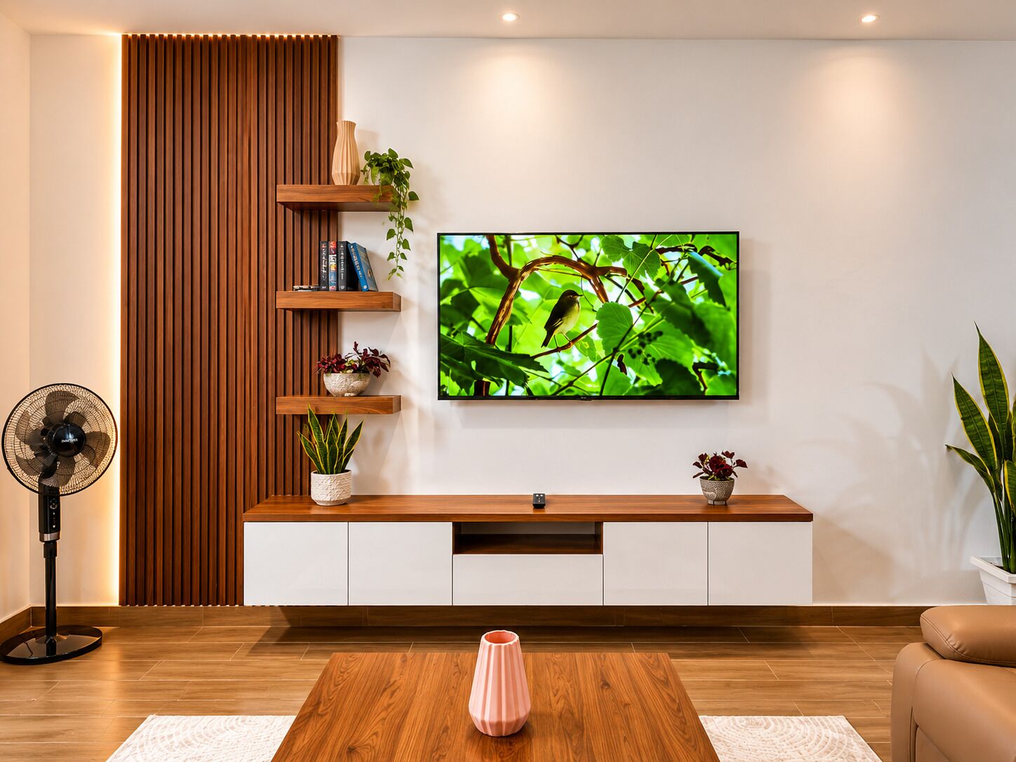 A modern living room with a flat-screen TV mounted on the wall, wooden shelves, a potted plant, a standing fan, and a coffee table.