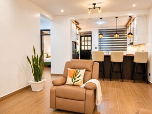 Una sala de estar moderna con un sofá de cuero, una planta en maceta y una zona de cocina con taburetes de bar.