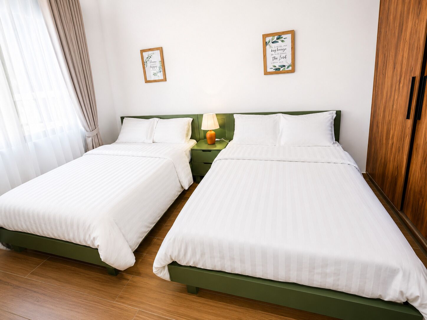 A hotel room with two single beds, a nightstand with a lamp, and two framed quotes on the wall.