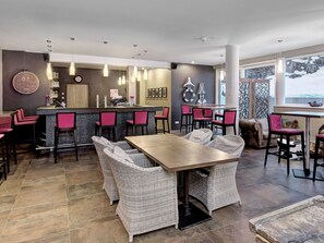 Una cocina moderna con asientos de bar, un comedor con mobiliario de mimbre y un amplio ventanal con vistas.