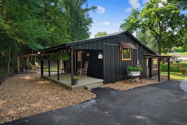 A rustic cabin with a covered porch, a small garden, and a gravel driveway.