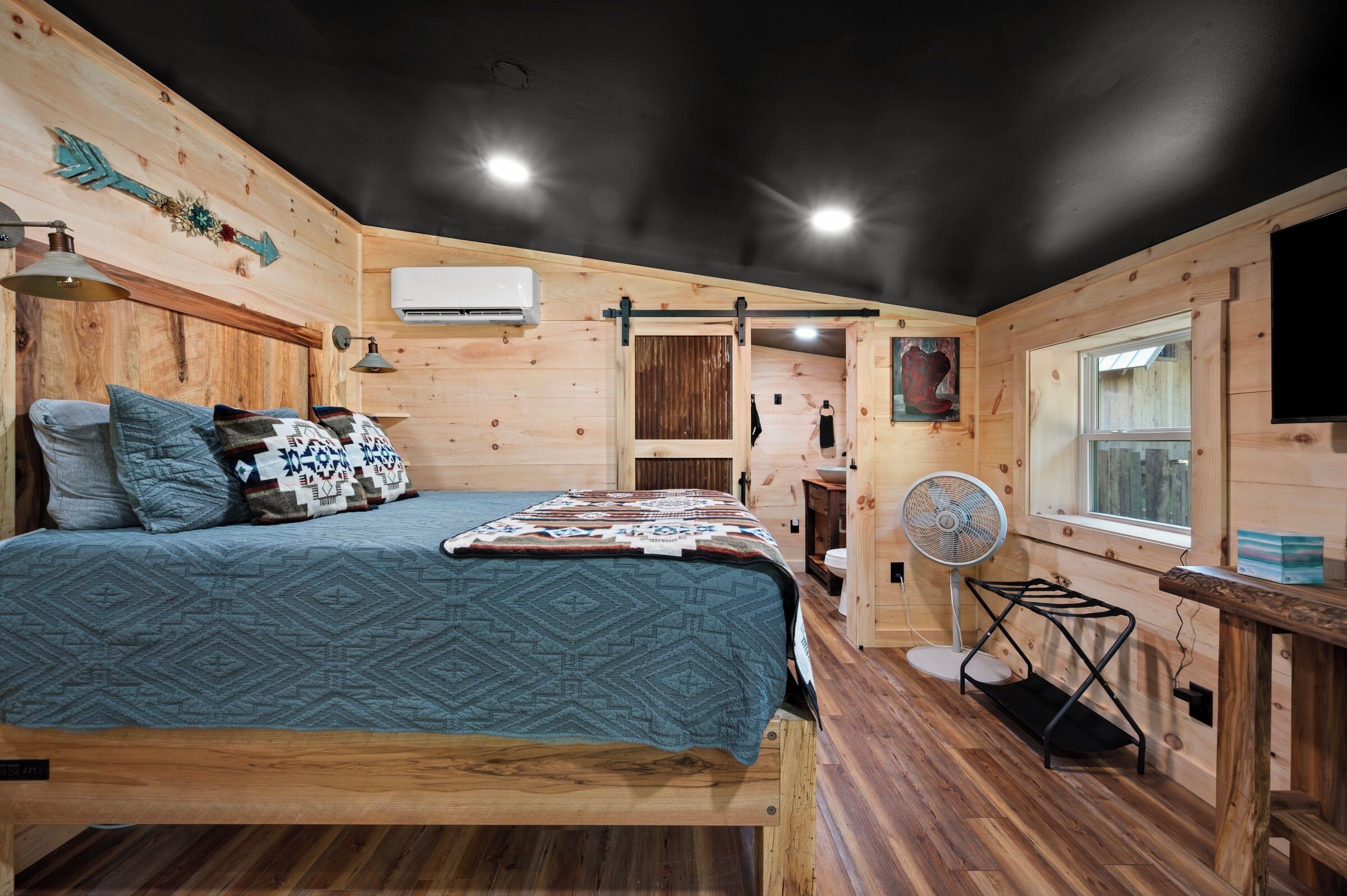 Interior de madera con una cama, un ventilador y una ventana.