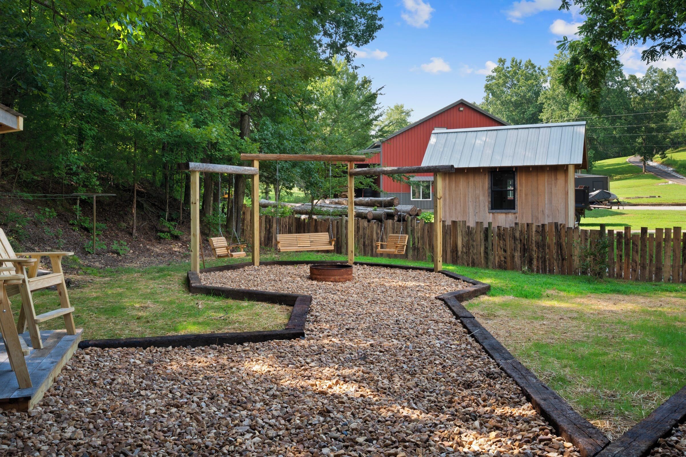 Un ensemble de balançoires en bois, un banc en bois et un bâtiment rouge avec un toit en métal, le tout dans un jardin.